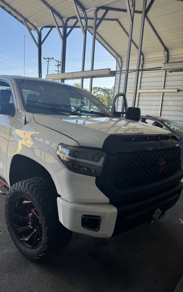 White pickup truck with black off-road wheels in an installation bay.
